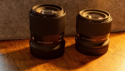Two prime lenses with gold-tinted optics displayed side by side on warm wooden surface.