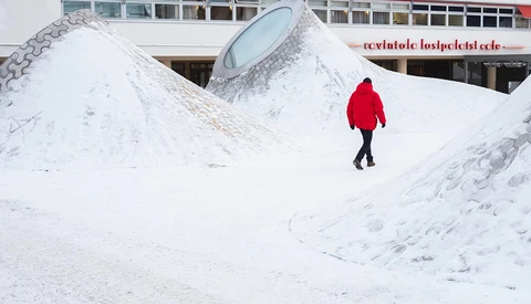 Person in bright red jacket walking across snowy landscape with geometric white structures.