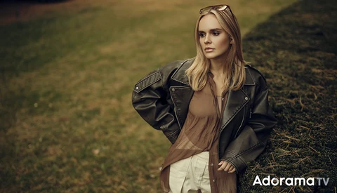 Woman in black leather jacket and neutral tones standing in overgrown field during golden hour.