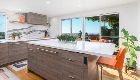 Modern kitchen with gray wood cabinetry, white quartz countertop, and large windows overlooking a landscape.