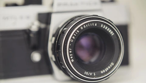 Vintage rangefinder camera with fast prime lens in sharp focus, blurred film camera body visible in background.