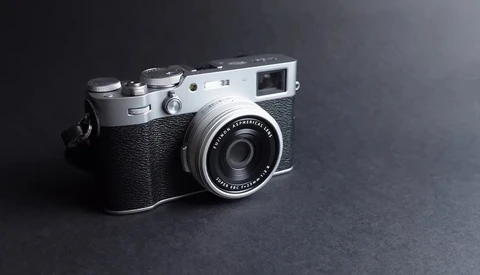 Fujifilm Instax rangefinder camera with silver top plate and black textured body against dark gray background.