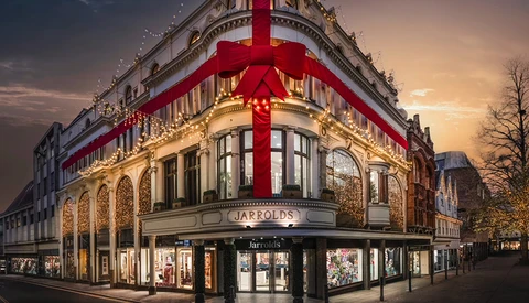 Historic corner building with ornate architecture illuminated at dusk, topped with large red ribbon bow.