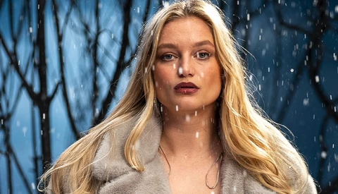 Woman with long blonde hair in falling snow against blue winter backdrop.