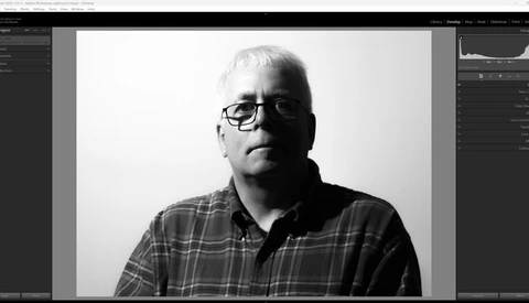 Black and white portrait of a man wearing glasses and a plaid shirt against a plain background.