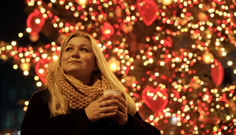 Woman gazing upward beneath warm bokeh holiday lights in red and gold tones.