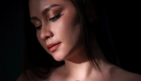 Woman's face in profile with warm golden eyeshadow and subtle lighting against dark background.