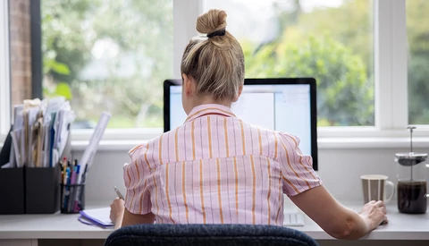 Person working at desk facing computer monitor with natural window light streaming in.