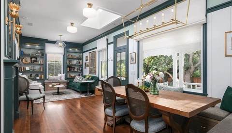 Modern home office with dark teal walls, wooden desk, and large windows overlooking gardens.