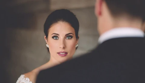 Bride in white lace wedding dress gazing at groom during intimate ceremony moment.