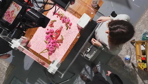 Overhead view of photographer working on pink fabric with floral arrangement during product shoot.