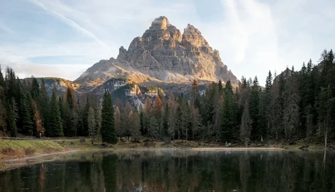 Jagged mountain peak reflected in still lake surrounded by coniferous forest.