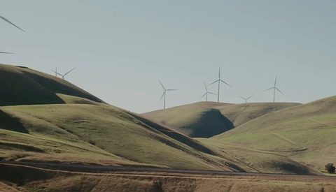 Rolling hills with wind turbines on distant ridge under overcast sky.