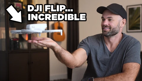 Man holding a small drone while gesturing toward it in an indoor setting.