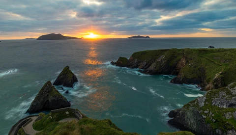 Dramatic sunset over dramatic coastal cliffs with turquoise waters and distant islands on the horizon.