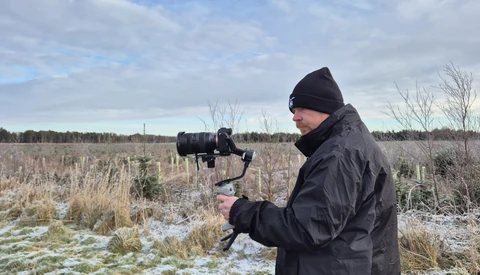 Videographer operating a camera mounted on a gimbal stabilizer in a snowy field.