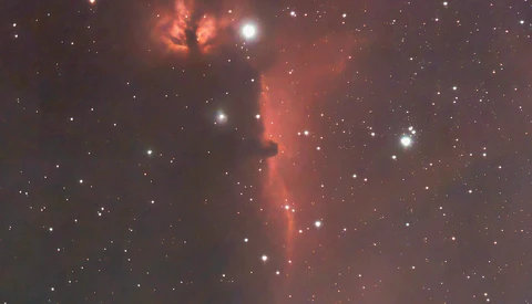 Deep-space photograph of an emission nebula with glowing red hydrogen gas clouds and scattered stars.