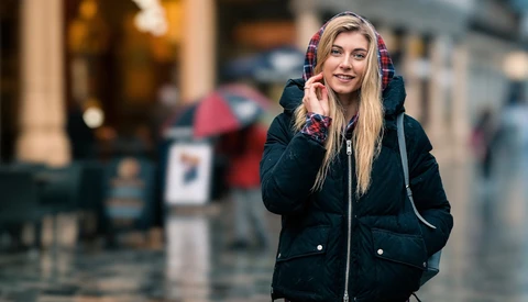 Woman in black winter jacket with colorful plaid hood talking on phone outdoors.