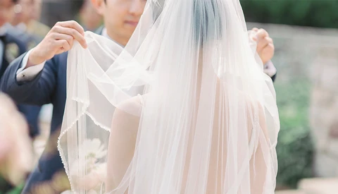 Groom adjusting bride's flowing veil during wedding ceremony.