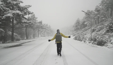 Runner in yellow jacket jogging down a snow-covered tree-lined road with arms outstretched.