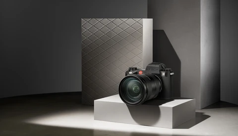 Professional mirrorless camera with telephoto lens displayed on white pedestal in minimalist studio setting.