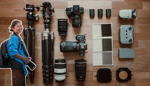 Photographer in blue jacket with complete camera gear laid out flat on wooden surface.