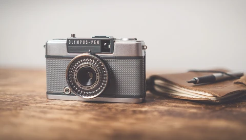 Olympus-Pen vintage film camera with textured silver body and black top plate on wooden surface.