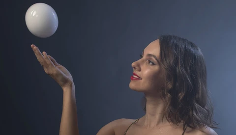 Woman in profile tosses a white sphere upward against a dark blue background.
