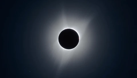 Total solar eclipse with moon silhouette centered against bright corona and darkened sky.