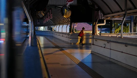 Lone figure in orange jacket standing on empty transit platform beneath arched ceiling.