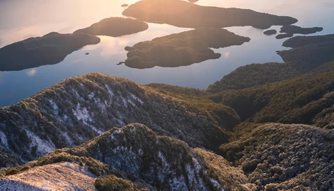 Forested mountains and islands at golden hour with still water reflecting the sky.