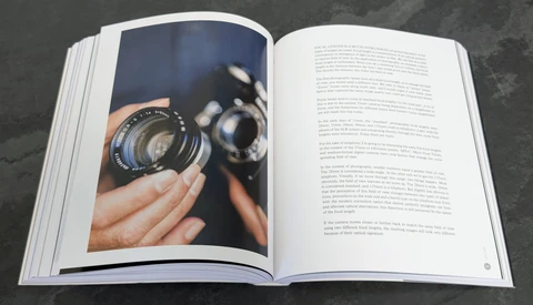 Open book displaying a photograph of hands holding a vintage camera lens on the left page, with text on the right.