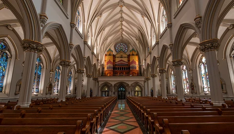 Interior of a Gothic cathedral with soaring vaulted ceilings, ornate pipe organ, and stained glass windows lining both sides.