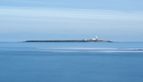 Small lighthouse on a rocky island beneath a clear blue sky and calm sea.