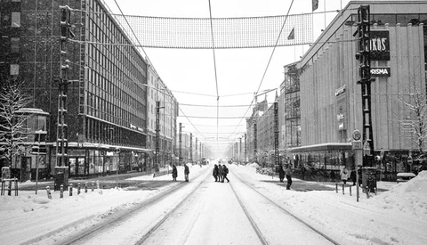 Snow-covered street with tram tracks stretching between tall residential buildings and storefronts.
