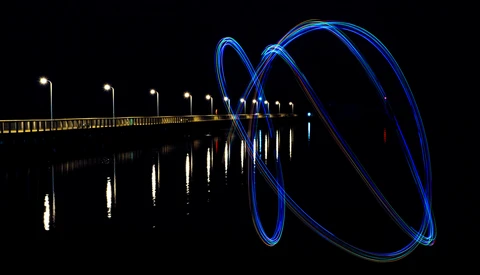Long exposure photograph of a pier at night with blue light trails spiraling from its end.