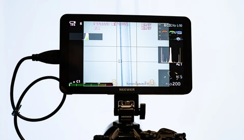 Neewer monitor mounted on tripod head displaying waveform and histogram data during video recording.