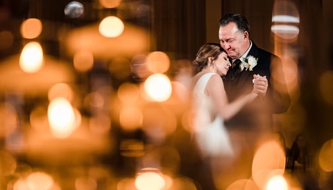 Bride and groom dancing together with warm bokeh lights in the background.