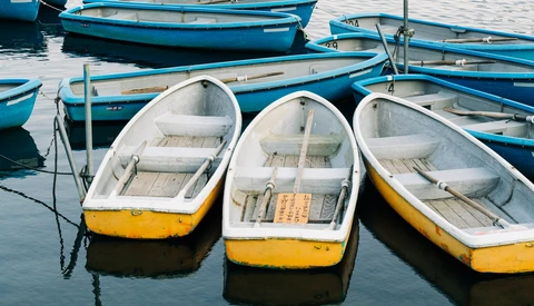 Three white and yellow fishing boats moored in calm blue water, with additional blue boats visible in the background.