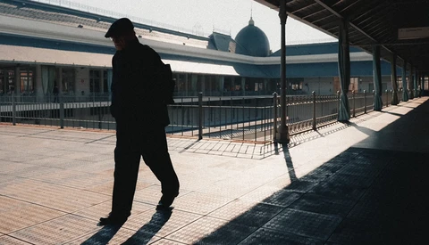 Silhouetted figure walking on a sunny rooftop terrace with architectural elements in background.