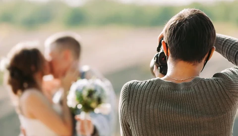 Wedding photographer capturing a bride and groom outdoors with a telephoto lens.