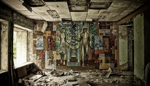 Abandoned interior room with deteriorating murals on walls and ceiling amid scattered debris and rubble.