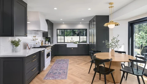 Modern kitchen with black cabinetry, white countertops, and wood dining table in open floor plan.