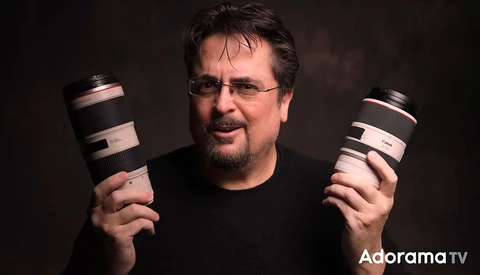 Photographer holding two telephoto lenses against a dark background.