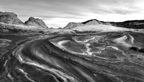 Sweeping curves of light and shadow flow across a vast volcanic landscape with distant mountains under stormy skies.