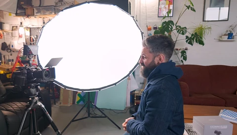 Photographer positioned beside large circular softbox reflector mounted on tripod during studio session.
