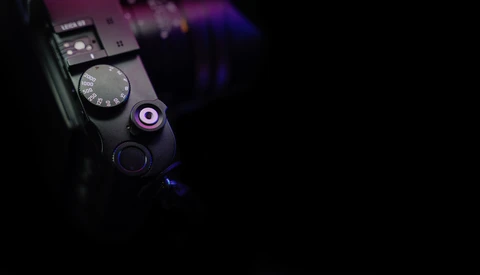 Close-up of a camera's top plate showing mode dial, shutter button, and illuminated control elements against a dark background.