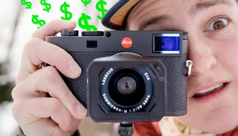 Photographer holding a Leica rangefinder camera with a small LCD screen visible on top.