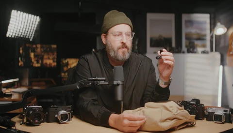 Photographer in studio holding camera gear while discussing equipment setup and techniques.
