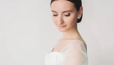 Woman in white off-shoulder dress photographed in profile against neutral background.